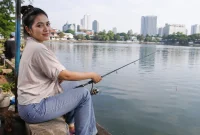 Seorang perempuan sedang memancing di pinggir danau.