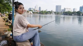Seorang perempuan sedang memancing di pinggir danau.