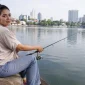 Seorang perempuan sedang memancing di pinggir danau.