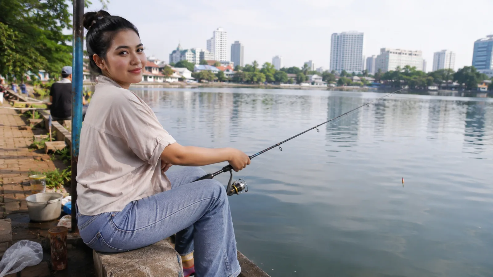 Seorang perempuan sedang memancing di pinggir danau.